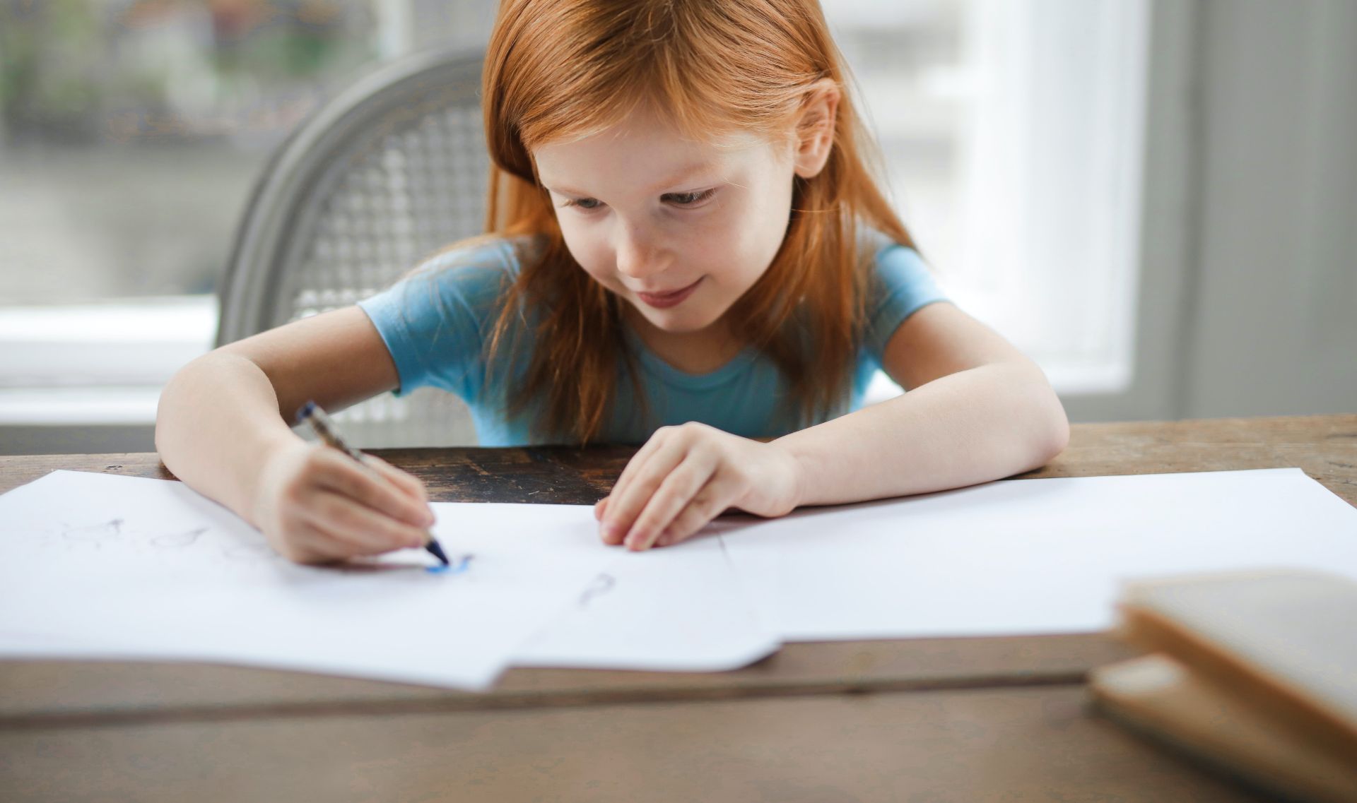 Diligent small girl drawing on paper in light living room at home