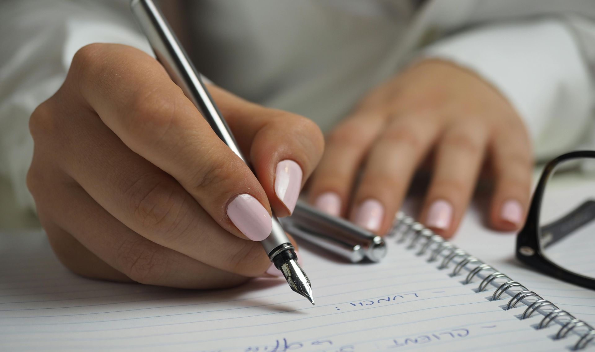 A detailed image of handwriting in a notebook with a fountain pen and glasses, ideal for office themes.